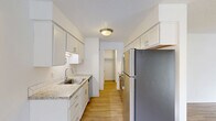 Located at 7850 SW Hall Blvd in Beaverton, Oregon, this two-bedroom, one-bathroom residence offers a well-designed single-floor layout. The galley-style kitchen is a functional highlight, featuring white shaker cabinetry, granite-look countertops, a subway tile backsplash, stainless steel appliances including a refrigerator and dishwasher, and a black electric range. Ample upper and lower cabinet storage makes this kitchen both practical and visually clean.

The living room is bright and open, with light wood-look flooring, a textured ceiling, a baseboard heating unit, and a sliding glass door that opens to a private balcony with greenery views, filling the space with natural light.

The two bedrooms offer distinct flooring options — one with plush carpet and a window with vertical blinds, and one with wood-look flooring — both equipped with baseboard heaters. The primary bedroom includes a walk-in closet visible from the kitchen hallway.

The bathroom is neatly appointed with a white vanity, granite-look countertop, and a large mirror. Consistent white walls and textured ceilings throughout lend a cohesive, clean aesthetic to the entire unit.