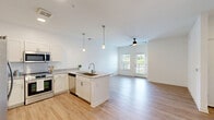 Located at 14055 Central Loop in Woodbridge, VA, this well-appointed one-bedroom, one-bathroom residence offers a thoughtfully designed single-floor layout. The open-concept kitchen and living area serves as the heart of the home, featuring crisp white cabinetry, granite countertops, a central island with a undermount sink, stainless steel appliances — including a French door refrigerator, microwave, dishwasher, and range — and elegant pendant lighting. Light wood-style flooring runs throughout, enhancing the bright, airy atmosphere created by the white walls and natural light. The living area is anchored by a ceiling fan and opens directly to a private balcony with outdoor views of the surrounding green space. The bedroom is a comfortable, well-sized retreat with clean lines and easy access to the hallway. The bathroom features a white vanity with granite countertops, a large mirror, and ample storage. A walk-in closet with wire shelving provides generous storage capacity, complemented by two additional closets. An in-unit laundry area adds everyday convenience. The overall design is modern and clean, with a neutral palette that creates a welcoming, move-in-ready environment.
