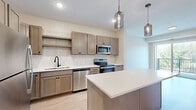 Located at 6701 W 78th St in Bloomington, MN, this one-bedroom, one-bathroom unit offers a well-designed layout across a single floor. The kitchen serves as a standout feature, showcasing taupe Shaker-style cabinetry, a tile backsplash, light quartz countertops, and a full suite of stainless steel appliances including a refrigerator, range, microwave, and dishwasher. A central island with pendant lighting adds both function and style, while light hardwood-style flooring ties the space together seamlessly.

The living area extends naturally from the kitchen and opens to a private balcony through sliding glass doors, bringing in ample natural light and outdoor views of surrounding greenery. The bedroom is a comfortable size, featuring plush carpet, large windows that frame tree-lined views, and a dedicated closet for storage.

The bathroom is cleanly appointed with a vanity featuring taupe cabinetry, a tub-shower combination, and black accent hardware that adds a modern touch. Consistent hardwood-style flooring flows through the main areas, while soft carpet lines the bedroom. The overall aesthetic is modern and cohesive, with neutral tones, clean lines, and quality finishes throughout.
