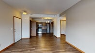 Located at 8808 North Indian Trail Road in Spokane, Washington, this single-floor unit offers a well-designed, open-concept layout that balances functionality with modern aesthetics. Rich, dark hardwood-style flooring flows throughout the main living areas, complementing the neutral gray walls and warm wood trim accents that frame doorways and baseboards throughout the space.

The living area is generously sized, featuring a glass-panel entry door that allows natural light to filter in alongside a large adjacent window, offering views of the surrounding neighborhood. The open layout transitions seamlessly into the kitchen, which is equipped with dark espresso-toned cabinetry, granite-style countertops, a classic subway tile backsplash, and a full suite of stainless steel appliances including a range, microwave, refrigerator, and dishwasher.

The bedrooms feature plush carpeting and large windows that bring in ample natural light while providing outdoor views. Sliding wood-paneled closet doors add a cohesive design element to each room. The bathrooms are finished with dark vanity cabinetry, stone-look countertops, tile backsplashes, and chrome fixtures, maintaining a consistent contemporary style throughout the unit.