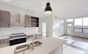 This contemporary single-floor unit showcases a clean, modern design characterized by crisp white walls, light-toned luxury vinyl plank flooring, and an abundance of natural light throughout. The open-concept living and dining area flows seamlessly toward a private balcony accessible through a glass-panel door, framing pleasant views of the surrounding neighborhood.

The kitchen is a standout feature, offering a generous island with a quartz countertop, an undermount stainless steel sink, and stylish dark pendant lighting overhead. Two-tone cabinetry in warm wood and grey tones pairs with a textured white tile backsplash, while stainless steel appliances — including a refrigerator, electric range, and ventilation hood — complete the well-appointed cooking space.

The bedrooms are bright and well-proportioned, each benefiting from large windows that capture open sky views and fill the rooms with natural light. The bathrooms are thoughtfully designed; one features accessibility grab bars alongside a white vanity with a quartz top and a large mirror, while a second bathroom includes a full soaking tub with a shower and brushed gold fixtures. The overall ambiance of the unit is fresh, airy, and move-in ready, with a cohesive modern aesthetic carried throughout every room.