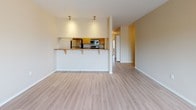 This single-floor residence features a thoughtfully designed open-concept layout with light-toned luxury vinyl plank flooring throughout the main living areas and kitchen. The living space flows seamlessly into the kitchen, which is separated by a raised breakfast bar with granite-style countertops and pendant lighting overhead, providing both a casual dining option and a natural visual divider. The kitchen is well-appointed with warm wood cabinetry, stainless steel appliances including a refrigerator, electric range, and over-the-range microwave, along with matching granite-style countertops and a utility sink.

The bedrooms are carpeted in neutral tones and offer generous natural light through slatted blinds. The primary bedroom is notably spacious and features dual sliding closets, providing substantial storage. Additional bedrooms are similarly bright and well-proportioned.

Two bathrooms serve the unit; one features a tub-shower combination with a wood-cabinet vanity and granite-style countertop, while the second offers a streamlined vanity setup with matching finishes. A wall-mounted HVAC unit ensures independent climate control. The warm beige palette and consistent finishes throughout create a cohesive, clean aesthetic.