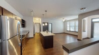 Located at 7210 Reading Rd in Rosenberg, TX, this single-floor residence offers a thoughtfully designed open-concept layout that seamlessly connects the kitchen, dining, and living areas. The kitchen is a standout feature, showcasing rich dark cabinetry, granite countertops, a central island with pendant lighting above, and a full suite of stainless steel appliances including a refrigerator, range, and built-in microwave. A built-in wine rack adds a refined touch to the cabinetry. Wood-style flooring extends throughout the main living areas, complementing the warm, contemporary aesthetic. Ceiling fans are installed in both the kitchen and living areas, enhancing comfort. The living space is bright and open, benefiting from natural light through windows fitted with white horizontal blinds. Bedrooms are carpeted and equipped with ceiling fans, offering a comfortable and quiet retreat, each with windows that bring in natural light. The bathroom features dark cabinetry with a granite-topped vanity, a large mirror, and wood-style flooring consistent with the rest of the home. The overall design balances modern finishes with functional, everyday living in a clean and cohesive interior palette.
