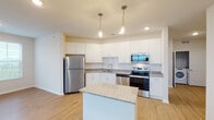 This single-floor residence offers a thoughtfully designed layout that balances functionality and comfort throughout its interconnected spaces. The kitchen serves as a central highlight, showcasing crisp white cabinetry, granite countertops, a subway tile backsplash, and a full suite of stainless steel appliances, including a refrigerator, range, microwave, and dishwasher. A freestanding center island with a matching granite surface provides additional workspace and a natural gathering point. Pendant lighting overhead adds a contemporary touch to the kitchen's clean aesthetic. Light-toned hardwood-style flooring extends through the kitchen and into the open living areas, creating a cohesive and airy feel. The living space benefits from multiple windows fitted with horizontal blinds, allowing natural light to filter in freely. Bedrooms feature plush carpeting and generous windows that introduce additional natural light. At least one bedroom connects directly to an en-suite bathroom equipped with a dual-sink granite vanity, a walk-in shower, and access to a walk-in closet. A secondary bathroom also features granite countertops and white cabinetry. Throughout, the neutral color palette and consistent finishes contribute to a clean, modern ambiance.