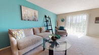This single-floor residence offers a thoughtfully arranged layout that balances comfort and functionality across its key living areas. The galley-style kitchen is a standout feature, equipped with white cabinetry, granite-style countertops, a mosaic tile backsplash, hardwood flooring, and a full suite of appliances including a dishwasher and range. The kitchen flows naturally into a dedicated dining area, which is brightened by a sliding glass door and accented by a pendant chandelier overhead, creating an inviting space for meals and gatherings. The living room makes a bold visual statement with a vibrant teal accent wall, plush carpeting, and access to natural light through vertical blinds, contributing to a warm and lively atmosphere. Two bedrooms continue the calming teal color palette, each featuring soft carpet, ceiling fans, closet storage, and sliding door access that allows natural light to fill the rooms. The full bathroom is clean and functional, featuring a tub-shower combination, a white vanity with storage, and wood-look flooring that adds a touch of warmth. Throughout the residence, a cohesive use of soft, neutral tones paired with vibrant accent walls creates a welcoming and stylish environment.