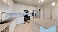 Located at 310 N Cattlemen Rd in Sarasota, Florida, this single-floor residence offers a clean, modern aesthetic with a thoughtfully designed open-concept layout. The kitchen is a standout feature, boasting white shaker-style cabinetry extending to the ceiling, a white subway tile backsplash, neutral quartz countertops, a full suite of stainless steel appliances including a French door refrigerator with ice maker, electric range, over-the-range microwave, and dishwasher. A spacious island provides additional prep and seating space, while pendant lighting adds a refined touch overhead. Light wood-look flooring flows throughout the main living areas, complementing the soft, neutral wall tones that create a bright and airy ambiance. The expansive living area benefits from recessed lighting and a ceiling fan, and opens seamlessly from the kitchen. Bedrooms are carpeted for comfort, with multiple windows dressed in horizontal blinds that allow natural light to filter in. The primary bedroom features dual windows offering exterior views and access to a walk-in closet. Bathrooms include white cabinetry, neutral countertops, and light wood-look flooring, with one bathroom offering built-in shelving storage. A smart thermostat is also present, adding a layer of modern convenience throughout this well-finished Sarasota residence.