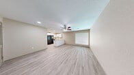This single-floor residence offers a clean, modern aesthetic defined by light-toned luxury vinyl plank flooring and warm neutral walls that flow consistently throughout the entire space. The open-concept living and dining area is generously proportioned, bathed in natural light through large windows fitted with white horizontal blinds. A ceiling fan with integrated lighting anchors the living space, enhancing both comfort and airflow. The kitchen is thoughtfully designed with crisp white shaker-style cabinetry, light granite countertops, a stainless steel sink, and black appliances including a refrigerator, range, and dishwasher. A peninsula counter creates a natural divide between the kitchen and living area while providing additional workspace. The bedrooms are well-sized, each featuring natural light from windows with blinds and ceiling fans in select rooms. One bedroom includes a louvered double-door closet alongside a six-panel door for added storage. The bathroom is elegantly finished with white cabinetry, granite countertops, a full tub-shower combination clad in large-format gray tile with a built-in niche, and light wood-look flooring. Recessed lighting and a textured ceiling complete the refined, move-in-ready interior throughout.