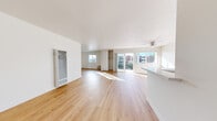This thoughtfully designed single-floor unit showcases a clean, modern aesthetic throughout, anchored by warm light hardwood flooring that flows seamlessly across every room. The expansive open-plan living and dining area is the centerpiece of the space, bathed in natural light through large windows and wide sliding glass doors that lead to a private balcony with outdoor views. A ceiling fan adds practical comfort to the living area, while a built-in wardrobe with open shelving provides convenient storage.

The kitchen is both functional and stylish, featuring white shaker cabinetry extending to the ceiling, light quartz countertops, a stainless steel gas range, and a peninsula with a sink that opens directly to the living area—ideal for everyday living and entertaining alike.

The bedroom is a serene, sun-filled retreat with a large window framing tree and street views, and is served by a dedicated bathroom complete with a full soaking tub and shower combo finished in clean white. An additional room, accessible via a bright hallway, offers flexible use and connects to a second bathroom vanity area. Throughout, crisp white walls and an abundance of natural light contribute to an airy, welcoming ambiance.