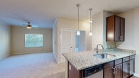 Located at 1001 Aventine Dr in Arden, NC, this well-appointed 2-bedroom, 2-bathroom single-floor residence offers a thoughtful layout designed for comfortable everyday living. The kitchen serves as a central highlight, showcasing rich dark wood cabinetry, granite countertops, a peninsula island with a stainless steel undermount sink, and a suite of stainless steel appliances including a refrigerator, electric range, microwave, and dishwasher. Stylish pendant lighting illuminates the island, while track lighting and hardwood-style flooring complete the kitchen's polished look. An adjacent pantry provides additional storage. The open flow connects the kitchen to the living room, which features plush carpeting, crown molding, and a ceiling fan. Both bedrooms are carpeted and equipped with ceiling fans, offering a comfortable retreat. The primary bedroom includes mirrored sliding closet doors and a wide window framing views of surrounding greenery. The secondary bedroom also benefits from natural light and access to a closet. The two bathrooms are finished with light countertops and dark wood vanities; one bathroom features a jetted soaking tub with a tiled surround. With four closets throughout and a dedicated hallway, storage and circulation are well addressed in this efficiently designed home.