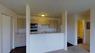 This 2-bedroom, single-floor residence offers a functional and straightforward layout designed for comfortable everyday living. The kitchen is a notable feature, defined by a raised pass-through counter that visually connects it to the adjacent living area while maintaining a sense of separation. Light-toned cabinetry lines the walls, providing ample storage space, and the kitchen comes equipped with standard appliances including a range, built-in microwave, and refrigerator. A sink is conveniently positioned along the pass-through counter, making the space practical for both cooking and entertaining. Structural columns frame the kitchen opening, adding architectural definition to the layout. The living area features neutral carpet flooring, contributing to a warm and understated atmosphere throughout. The overall color palette remains light and neutral, with white walls and beige tones that create a clean, open feel. The single-floor design ensures easy accessibility and a cohesive flow between spaces, making this a practical and well-organized residence suited for a variety of lifestyles.