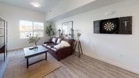 This well-appointed single-floor residence offers a thoughtfully designed layout that balances modern aesthetics with everyday functionality. The open kitchen is a standout feature, showcasing crisp white cabinetry with brushed nickel hardware, white quartz countertops, a subway tile backsplash, and a full suite of stainless steel appliances including a range, over-the-range microwave, and refrigerator. A central island with bar seating provides additional workspace and a casual dining option, while pendant lighting adds a contemporary touch overhead.

The living area is bright and welcoming, with large windows that draw in natural light and warm wood-look luxury vinyl plank flooring underfoot. The space is versatile and features a wall-mounted dartboard, adding a recreational element to the room.

Two bedrooms offer comfortable retreats, each with plush carpet flooring. The primary bedroom connects directly to a bathroom that opens into a walk-in closet with wire shelving, providing generous storage. Both bathrooms are finished with white cabinetry, quartz countertops, matching brushed nickel hardware, and tub-shower combinations. The clean, neutral palette throughout the residence creates a cohesive and modern living environment.