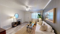 This single-story, 1-bedroom, 1-bathroom residence offers a thoughtfully organized layout that maximizes everyday functionality. The inviting living room serves as the heart of the home, featuring light wood-style flooring, crown molding, a textured ceiling with a ceiling fan, and a striking dark accent wall with vertical wood paneling. Natural light filters through windows dressed with sheer curtains, creating a bright and welcoming atmosphere. An additional carpeted room with large windows provides flexible space suitable for use as an office or secondary sitting area. The bedroom offers plush carpeting, crown molding, and ample natural light through a curtained window, providing a calm and restful retreat. Three closets throughout the unit ensure generous storage capacity. The kitchen includes a full-size refrigerator and an adjoining dining area with wood-style flooring, crown molding, and a secondary exterior door. The full bathroom features a shower-tub combination. A dedicated laundry space adds practical convenience. Throughout the home, consistent crown molding, neutral tones, and durable flooring materials contribute to a cohesive and comfortable living environment suited for a variety of lifestyles.
