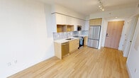 Located on the fifth floor at 5700 Biscayne Blvd in Miami's vibrant MiMo district, this contemporary studio unit offers a thoughtfully designed open-plan layout combining the kitchen and living area into a single, efficient space. Light-toned hardwood flooring runs throughout, lending warmth and continuity to the interior.

The kitchen is outfitted with modern flat-front cabinetry in a two-tone finish — white uppers paired with natural wood lowers — complemented by a subway-tile backsplash and clean white countertops. A full suite of stainless steel appliances includes a French door refrigerator, electric range, built-in microwave, and dishwasher. Track lighting overhead provides focused illumination across the cooking and prep areas.

The living space is bright and open, with crisp white walls and an airy feel. A standout feature is the expansive floor-to-ceiling window wall that frames a lush, tree-lined outdoor view, flooding the interior with abundant natural light. The minimalist design of the space allows for flexible furniture arrangements.

A separate room, accessible via a clean white interior door, offers additional privacy and functions as a bedroom, also benefiting from the large windows and natural greenery views. The overall aesthetic is clean, modern, and well-suited to urban living in Miami.