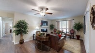 Located at 7939 Waters Ave in Savannah, Georgia, this single-story residence offers a well-appointed and cohesive living environment with warm, neutral tones throughout. The living room serves as the centerpiece of the home, showcasing rich hardwood flooring, a classic fireplace with a white mantel, a ceiling fan, and windows that allow natural light to fill the space, creating a welcoming ambiance. Adjacent to the living area, the dining room features matching hardwood floors, a pendant light fixture, and wall-mounted décor accents that add character to the space. The kitchen is equipped with dark cabinetry, granite-style countertops, stainless steel appliances including an electric range, and a tile backsplash, offering both functionality and style. The bedroom is generously proportioned with plush carpeting, a large window with views of the surrounding greenery, and ample room for full bedroom furnishings. The bathroom provides a tub-shower combination, dark vanity cabinetry, and granite countertops consistent with the home's design palette. A dedicated laundry room accommodates full-sized washer and dryer units with overhead shelving for additional storage. Hardwood-style flooring flows consistently through the main living areas, tying the home's interior together cohesively.