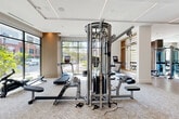 Located at 2120 Dunavant St in Charlotte's South End neighborhood, this expansive fitness center is a single-level facility offering a comprehensive and thoughtfully designed workout environment. The space is organized into distinct functional zones, each catering to different aspects of physical training.

Floor-to-ceiling windows line multiple walls, flooding the interior with natural light and providing open views of the surrounding neighborhood streetscape. The generous footprint accommodates a wide array of Matrix cardio equipment — including treadmills, stair climbers, stationary bikes, and rowing machines — arranged to take full advantage of the natural light and outdoor views.

A dedicated strength training area features a multi-station cable machine, adjustable benches, and a full dumbbell rack, all set on light hardwood flooring. Warm wood-slatted architectural accents and a striking large-scale textured wall mural add visual interest and a refined aesthetic throughout. Recessed lighting and linear LED fixtures illuminate the space evenly.

A separate open studio area with light hardwood floors, sheer drapery, and a stone-clad accent wall offers a clean, serene environment ideal for stretching, yoga, or personal training. A wall-mounted flat-screen display and built-in cabinetry provide added functionality. The overall design strikes a balance between high-performance utility and modern, upscale aesthetics.