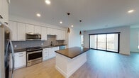 Located at 4305 Third Ave in San Diego, this single-floor unit offers a well-designed open-concept layout with modern finishes throughout. The kitchen serves as a central highlight, featuring floor-to-ceiling white cabinetry, stainless steel appliances including a gas range, built-in microwave, and refrigerator, complemented by a decorative geometric tile backsplash and dark countertops. Copper-toned pendant lights hang above a large central island, adding a warm contrast to the clean white palette. Light wood-tone flooring extends through the kitchen and living areas, creating a cohesive and airy feel. The living area is generously proportioned, with recessed lighting and sliding glass doors leading to a private balcony with outdoor views. The bedroom features neutral carpet and bright white walls, offering a calm and restful environment. Two bathrooms are finished with consistent design elements, including dark-countered white vanities, matte black hardware, large mirrors, and tile flooring. One bathroom offers additional built-in cabinetry for storage. Recessed lighting throughout maintains a clean, contemporary ambiance across the entire unit.