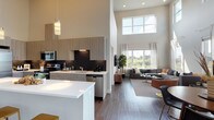 This contemporary two-story residence makes a striking first impression with its dramatic double-height ceilings in the open-concept main living area. The kitchen is a standout, featuring light wood-grain cabinetry extending to lofted heights, a dark subway tile backsplash, stainless steel appliances, and a large white quartz island that flows seamlessly into the dining and living spaces. Hardwood-style flooring runs throughout the main level, anchoring the bright, airy atmosphere created by expansive windows that frame sweeping views of open meadows and tree canopies beyond.

The living room benefits from abundant natural light, with oversized windows and sheer drapery enhancing the connection to the outdoors. The primary bedroom suite includes a generous walk-in closet with built-in organizers and an en-suite bathroom with dual sinks, a wide quartz vanity, and wood-grain cabinetry. An additional bedroom offers plush carpet flooring, a bold accent wall, and natural views through large windows. A second full bathroom features dark tile surround in the tub/shower combination and matching cabinetry finishes.

The upper level provides a versatile loft-style bonus room with carpet, a closet, and a built-in desk area—ideal as a home office or lounge. Throughout, the design balances modern finishes with a warm, livable aesthetic.