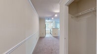 Located at 50 Greenleaf Rd in Conyers, GA, this single-floor, one-bedroom, one-bathroom home offers a functional and comfortable layout. The living room is a bright, open space featuring plush carpeting, crown molding, and an abundance of natural light from large windows with views of surrounding greenery, as well as a glass-paned exterior door providing direct outdoor access. The space flows seamlessly into the kitchen via a pass-through breakfast bar, making the layout feel connected and practical. The galley-style kitchen is well-equipped with white cabinetry, light stone countertops, a stainless steel sink, and black appliances including a refrigerator, range, and dishwasher, all accented by light hardwood-style flooring and a window overlooking the outdoors. A carpeted hallway with crown molding and track lighting connects the main living areas to the private bedroom, which features soft carpeting, a ceiling fan, a generous walk-in closet with built-in shelving, and a window that fills the room with natural light. The bathroom includes a white vanity with ample counter space and warm hardwood-style flooring. Throughout, the home maintains a neutral, light-toned palette that creates a clean and welcoming ambiance.