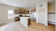 This single-story home is designed with a clean, contemporary aesthetic and a neutral color palette throughout. The kitchen serves as a central highlight, featuring dark taupe cabinetry with brushed hardware, crisp white countertops, and a full suite of stainless steel appliances including a range, microwave, dishwasher, and refrigerator. A center island provides additional workspace and visual separation, while light wood-look flooring ties the kitchen seamlessly into the adjacent living areas.

The living spaces are generously sized and filled with natural light, courtesy of multiple windows fitted with horizontal blinds. The open layout connects the main living area to the kitchen, creating an ideal flow for daily living. Recessed lighting and textured ceilings are consistent throughout the common areas.

The bedrooms feature neutral carpet, ceiling fans, and windows that bring in natural light. The bathroom includes a wide vanity with a white countertop, a large mirror, and a tub-shower combination. A built-in shelving nook near the entry provides convenient storage. Overall, the home presents a well-organized, move-in-ready layout with consistent finishes throughout.