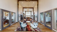 Located at 5000 Hutchison Street in Ashville, Ohio, this single-floor community clubhouse offers an expansive and thoughtfully designed gathering space. The main living area makes an immediate impression with its soaring ceilings, bold exposed wood beam accents, and warm hardwood flooring. A statement chandelier anchors the room, while large windows at the entryway flood the space with natural light and offer views of the surrounding greenery. Eclectic, western-inspired furnishings — including leather seating, cowhide-patterned accent chairs, and vibrant area rugs — lend the space a distinctive character. A linear fireplace and large-screen TV create a comfortable lounge zone, complemented by curated artwork displayed throughout.

A dedicated theater room provides a true cinematic experience, outfitted with rows of black leather reclining seats, a large projection screen, ambient LED lighting, patterned carpet, and a built-in beverage station. The fitness center is comprehensively equipped with treadmills, ellipticals, strength machines, free weights, and wall-mounted TVs, all set on durable rubber flooring with natural light provided by exterior-facing windows. A connecting hallway ties the spaces together, completing this well-appointed and versatile community facility.