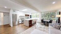 Located at 1267 N Laurel Ave in the heart of West Hollywood, this thoughtfully designed one-bedroom, one-bathroom residence delivers a clean, modern aesthetic across a well-appointed single floor. Warm hardwood flooring flows seamlessly throughout the living spaces, grounding the bright, white interior palette.

The open-concept living and dining area is anchored by recessed lighting and features a striking marble-top dining table that pairs naturally with the kitchen. The living room offers generous seating space and is highlighted by bold wall art, creating an inviting yet refined ambiance.

The chef's kitchen is a standout, outfitted with high-gloss white cabinetry, a dramatic marble-veined quartz island with bar seating, stainless steel professional-grade appliances, a gas range, and a deep undermount sink. A skylight bathes the kitchen in natural light, while a large window frames lush greenery beyond.

The bedroom is a serene retreat, featuring wide windows for natural light, wood-accented flooring, mirrored closet doors that amplify the sense of space, and direct access to a dedicated walk-in closet with built-in shelving.

The bathroom is spa-inspired, finished with large-format marble-look porcelain tile, a glass-enclosed shower, and a sleek floating vanity, all contributing to a clean, luxurious feel.