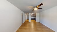 This single-floor residence offers a thoughtfully designed open-concept layout that connects the living area and kitchen seamlessly. The main living space features light-toned hardwood-style flooring, clean white walls, and a ceiling fan with integrated lighting, contributing to a bright and airy atmosphere. A window along the far wall allows natural light to filter in, offering views of surrounding greenery.

The kitchen is a standout feature, outfitted with dark shaker-style cabinetry, granite countertops, a subway tile backsplash, and a full suite of stainless steel appliances including a refrigerator, range, microwave, and dishwasher. Ample upper and lower cabinet storage makes this kitchen as functional as it is visually appealing.

A hallway connects the living areas to the bedrooms, one of which features plush carpeting, a ceiling fan, a walk-in closet, and a sliding barn-style door for added character. The primary bathroom includes a granite-topped vanity, tile flooring, and a tub-shower combination. A secondary bathroom offers a wood-toned vanity with a framed mirror. Throughout, the space maintains a clean, contemporary aesthetic with consistent finishes and a neutral color palette.
