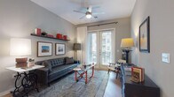 This thoughtfully designed 2-bedroom, 2-bathroom single-floor residence combines modern aesthetics with functional living. The open-concept living area features warm wood-look flooring, a ceiling fan, floating display shelves, and French doors that lead to a private balcony, filling the space with natural light and outdoor views. The kitchen is a standout, outfitted with stainless steel appliances, two-tone cabinetry — white uppers paired with gray lowers — white quartz countertops, a subway tile backsplash, a center island with open shelving, and pendant lighting. A stacked in-unit washer and dryer is conveniently tucked nearby. Both bedrooms offer plush carpeting, large windows with blinds and curtains, and ample space for comfortable furnishings. The primary bathroom features a long vanity with white cabinetry, gray countertops, and wood-look flooring, while the second bathroom includes a tub-shower combination and a matching vanity. Neutral gray walls throughout create a cohesive, calming palette that complements the contemporary finishes. The overall ambiance is modern, clean, and inviting, making this residence a well-rounded and stylish place to call home.