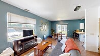 This two-story home offers a well-organized layout across two floors, with the majority of the living space situated on the main level. The living room is a welcoming area distinguished by bold teal-painted accent walls, warm hardwood-style flooring, and multiple windows that invite abundant natural light and outdoor views. The dining room adjoins the living area seamlessly and features a sliding glass door that opens to an outdoor view of a green lawn, enhancing the sense of openness. The kitchen is designed for practicality, featuring white cabinetry, ample counter space, and a galley-style layout that maximizes efficiency. Hardwood-style flooring continues throughout the main level, creating a cohesive feel. A staircase leads to the upper floor, where three carpeted bedrooms provide comfortable private retreats. The primary bedroom offers a cozy yet functional space with closet storage. The two bathrooms are functional and well-appointed, each featuring a shower-tub combination. Throughout the home, the consistent teal accent color scheme ties the common areas together, giving the space a distinct and cohesive character. The split layout across two floors provides a clear separation between living and sleeping areas.