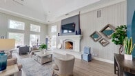 Harbor House on Saratoga's clubhouse is a thoughtfully designed, single-floor community space that blends coastal charm with modern comfort. The entrance makes an immediate impression with bold teal walls framing elegant arched doorways trimmed in silver, leading residents into the heart of the facility.

The main lounge is an expansive, light-filled gathering area anchored by a white-mantled fireplace with a mounted flat-screen television above it. Soaring ceilings, vertical shiplap-style wall paneling, and large windows flood the room with natural light while offering picturesque views of the outdoor pool and palm-lined surroundings. Neutral, contemporary furnishings create a relaxed yet refined atmosphere.

A dedicated game room continues the teal accent wall aesthetic and reaches equally impressive ceiling heights. It is equipped with a pool table, foosball table, and casual seating, with direct access to an outdoor patio area.

The refreshment bar area features white cabinetry with granite countertops, a gray subway tile backsplash, a beverage refrigerator, and a coffee station — all accented by coastal-themed framed artwork. Light wood-look flooring runs throughout the entire space, tying each area together cohesively.

Floor plan displays for Harbor House on Saratoga are prominently featured near the lounge windows, making this clubhouse equally functional as a leasing and community hub.