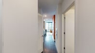 Located in Chicago's Lakeshore East neighborhood, this single-floor residence at 455 E Waterside Dr offers a thoughtfully designed living experience with contemporary finishes throughout. The entry hall, lined with louvered storage doors, leads into an open-plan living area anchored by a bold terracotta accent wall featuring a round mirror — a standout architectural detail that adds warmth and visual interest to the space.

The living area is bathed in natural light from expansive floor-to-ceiling windows and a sliding glass door that frames sweeping views of Lake Michigan, the marina, and neighboring high-rises. Dark hardwood flooring runs throughout, complementing the warm, mid-century modern furnishings.

The galley-style kitchen features wood-grain lower cabinetry, crisp white upper cabinets, a dark tile backsplash, stainless steel sink, and a gas range — combining style with functionality. The kitchen flows seamlessly toward the living space, maintaining an open and connected layout.

The sleeping area is partially enclosed, offering privacy while preserving the open feel of the home, and includes a closet with built-in shelving. The bathroom is clean and modern, equipped with a wood-finish vanity, illuminated mirror, walk-in glass shower, and dark stone tile flooring.