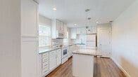 This single-floor, 2-bedroom, 2-bathroom home offers a thoughtfully designed layout with a clean, modern aesthetic. The kitchen is a standout feature, showcasing white shaker-style cabinetry, granite countertops, a central island with pendant lighting above, wood-look flooring, and white appliances including a range, microwave, and refrigerator. Natural light filters in through blinds-covered windows, enhancing the bright and airy feel of the space.

The living room provides a welcoming atmosphere, highlighted by a fireplace with a wood mantel and tile surround, plush carpeting, a ceiling fan, and vaulted ceilings that add a sense of openness. Both bedrooms are carpeted and naturally lit, with the primary bedroom offering a ceiling fan and a walk-in closet equipped with wire shelving for ample storage.

The bathrooms are finished consistently with granite-topped vanities, wood-look flooring, and tiled tub-shower combinations featuring classic white subway tile with contrasting grout — a clean, timeless look. A hallway connects the bedrooms and bathrooms, completing the functional single-floor floor plan. The overall design balances practicality with modern finishes, creating a comfortable and cohesive living environment throughout.