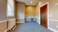 Located at 888 Delaware Ave in Buffalo, NY, this two-bedroom, one-bathroom unit offers a thoughtfully designed single-floor layout. Warm taupe walls paired with crisp white chair-rail molding and bright white baseboards lend a classic, cohesive aesthetic throughout the space. Plush gray carpet flows seamlessly across the bedrooms and main living areas, adding comfort underfoot.

The primary bedroom is generously proportioned, accommodating a full suite of furnishings with ease. It features a large window that draws in natural light and views of the surrounding neighborhood. A second bedroom, connected via a rich wood-paneled door, provides flexible use as a guest room or home office, complete with a stylish brass wall sconce.

A built-in kitchenette anchors one end of the unit, featuring light gray cabinetry, a countertop sink, and a compact stainless steel appliance — ideal for everyday convenience. An ornate iron security door with a glass pane serves as the main entry, offering both character and practicality.

The bathroom is a standout feature, showcasing floor-to-ceiling marble-look tile surrounding the tub and shower, a gray vanity with a white countertop, a large mirror with overhead lighting, and coordinating marble-look floor tile — delivering a clean, elegant finish that elevates the overall space.