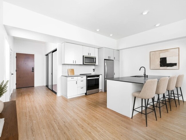 Cocina con encimeras de cuarzo, barra con asientos y armarios de diseño minimalista que se abre a una luminosa sala de estar con luz natural y acabados impecables. - Modera Bridle Trails