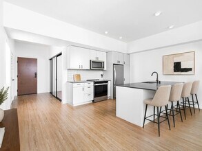 Kitchen with quartz countertops, bar seating, and streamlined cabinetry opening to a bright living area with natural light and clean finishes. - Modera Bridle Trails
