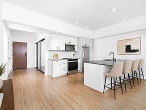 Kitchen with quartz countertops, bar seating, and streamlined cabinetry opening to a bright living area with natural light and clean finishes. - Modera Bridle Trails