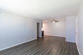 This single-floor unit offers a clean, neutral aesthetic with consistent wood-look flooring running throughout every room, creating a cohesive and easy-to-maintain living environment. The open living area is bright and spacious, benefiting from natural light through a window fitted with horizontal blinds. A textured ceiling adds character to the main living space, while a ceiling-mounted HVAC vent ensures year-round comfort. A hallway connects the living area to the rest of the unit, leading past the kitchen and into the private rooms beyond.

The kitchen is efficiently laid out with dark espresso-toned cabinetry providing ample storage above and below the counter. White appliances — including a gas range with a ventilation hood and a full-size refrigerator — complement the light countertops and keep the space feeling bright and functional.

The two bedrooms each feature the same wood-look flooring, neutral gray walls, and windows with blinds that allow for natural light and privacy. Both rooms are equipped with ceiling fans, supporting airflow and comfort. The bathroom is outfitted with a full tub-shower combination, brushed nickel hardware including grab bars, and continues the unit's clean, practical design language throughout.