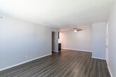 This single-floor unit offers a clean, neutral aesthetic with consistent wood-look flooring running throughout every room, creating a cohesive and easy-to-maintain living environment. The open living area is bright and spacious, benefiting from natural light through a window fitted with horizontal blinds. A textured ceiling adds character to the main living space, while a ceiling-mounted HVAC vent ensures year-round comfort. A hallway connects the living area to the rest of the unit, leading past the kitchen and into the private rooms beyond.

The kitchen is efficiently laid out with dark espresso-toned cabinetry providing ample storage above and below the counter. White appliances — including a gas range with a ventilation hood and a full-size refrigerator — complement the light countertops and keep the space feeling bright and functional.

The two bedrooms each feature the same wood-look flooring, neutral gray walls, and windows with blinds that allow for natural light and privacy. Both rooms are equipped with ceiling fans, supporting airflow and comfort. The bathroom is outfitted with a full tub-shower combination, brushed nickel hardware including grab bars, and continues the unit's clean, practical design language throughout.