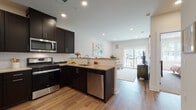 This single-floor residence offers a thoughtfully designed open-concept layout that seamlessly connects the kitchen, dining, and living areas. The kitchen is a standout feature, outfitted with rich dark espresso cabinetry, light stone countertops, a white subway tile backsplash, and a full suite of stainless steel appliances including a gas range, built-in microwave, and dishwasher. A peninsula with bar seating provides both additional prep space and a casual dining option. Warm hardwood-style flooring runs throughout the main living areas, adding continuity and warmth to the space. The living room is bright and inviting, anchored by large sliding glass doors that flood the room with natural light and provide views of the surrounding greenery. The bedroom is a comfortable retreat, featuring a generous window that draws in natural light and offers an open view of the outdoors. The bathroom is clean and well-appointed, with dark cabinetry, a light countertop, tiled flooring, and a full shower-tub combination with decorative tile accents. A dedicated laundry area includes a stacked washer and dryer unit alongside a water heater, adding practical convenience. Recessed lighting throughout enhances the modern, polished ambiance of this well-designed residence.