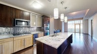 This thoughtfully designed 2-bedroom, 4-bathroom single-floor residence offers a refined living experience through its modern finishes and functional layout. Rich dark hardwood flooring flows through the main living areas, anchoring the open-concept design. The gourmet kitchen is a standout feature, showcasing a large central island with granite countertops, pendant lighting, stainless steel appliances including double wall ovens and a built-in microwave, a mosaic tile backsplash, and a mix of dark espresso and lighter wood cabinetry. The kitchen opens toward the living area, which is bathed in natural light from floor-to-ceiling windows offering sweeping city skyline views. The primary bedroom is generously proportioned with plush carpeting and direct access to an en-suite bathroom finished with large-format tile flooring, granite vanity, dark wood cabinetry, and a soaking tub. A custom walk-in closet features built-in shelving, hanging rods, and a multi-drawer dresser unit. The second bedroom also offers carpet flooring and large windows with city views. A powder room with a pedestal sink provides convenience for guests. Additional highlights include an in-unit laundry room with a front-load washer, a dedicated hallway, and two closets, completing this well-equipped and stylish urban residence.
