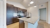 This thoughtfully designed 2-bedroom, 2-bathroom residence offers a comfortable and modern living experience across a single floor. Light wood flooring runs continuously throughout, creating a warm, cohesive aesthetic in every room.

The kitchen serves as a centerpiece of the home, featuring rich dark wood cabinetry extending to the ceiling for generous storage, a granite-topped island with an undermount sink and pendant lighting overhead, stainless steel appliances, and a subway tile backsplash. Vaulted ceilings above the kitchen add an impressive sense of openness to the space.

The living area flows naturally from the kitchen and includes ceiling fans for comfort. Two closets — including a spacious walk-in fitted with wire shelving systems — provide ample storage throughout the home.

Both bedrooms are bright and airy, with neutral walls and natural light admitted through window blinds. The primary bedroom is generously sized and accompanied by its own walk-in closet.

The bathrooms maintain the same design language as the kitchen, featuring dark wood vanities with granite countertops and undermount sinks. One bathroom includes a combination tub and shower with clean white tile surround.

A hallway with large double doors provides additional storage or utility space. Overall, the home presents a clean, modern aesthetic with consistent, quality finishes throughout.