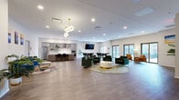 Located on Euclid Avenue in the heart of Cleveland, OH, this single-floor space offers a generously sized, open-concept layout that seamlessly blends a fully equipped kitchen with a comfortable living area. The kitchen is a standout feature, boasting a large central island with bar seating, crisp white countertops, warm wood-toned cabinetry, stainless steel appliances including a French door refrigerator and double wall oven, open shelving with decorative greenery, and a sleek wall-mounted range hood. Pendant lighting overhead adds a polished, modern touch.

The living area is bright and expansive, with light wood-style flooring running throughout the entire space. A wall-mounted fireplace beneath a large flat-screen TV creates a welcoming focal point, while a seating arrangement with leather accent chairs and a patterned area rug adds warmth. Large sliding glass doors flood the space with natural light and provide direct access to an outdoor patio area. An additional seating and dining zone with a wall-mounted TV offers versatile use for gatherings or events.

The entry area is clean and minimal, featuring a statement globe chandelier, colorful artwork, and lush potted plants that add life and personality. Recessed lighting throughout ensures a bright, welcoming ambiance across the entire floor.