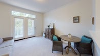Located at 6110 Riverwoods Dr in Wilmington, North Carolina, this single-floor residence offers a well-organized layout designed for comfortable everyday living. The kitchen is equipped with essential appliances, including an electric range with overhead microwave and warm wood cabinetry, all finished with light tile flooring that extends into the adjacent laundry area. A dedicated in-unit laundry closet conveniently houses a full-size washer and dryer, adding a practical touch to the home. Crown molding accents the living and dining area, which is brightened by natural light streaming through a set of French doors flanked by transom windows. The space opens to an outdoor view framed by lush greenery, creating an airy and inviting atmosphere. Soft carpet flooring flows throughout the living area and bedroom, lending warmth underfoot. The bedroom is a serene retreat, featuring a large window that draws in natural light and provides views of the surrounding landscape, along with ample space for a dresser and additional furnishings. The bathroom is cleanly appointed with tile flooring, a wood-cabinet vanity, large mirror, and well-lit vanity lighting above, completing this move-in ready residence.
