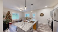 Located in River Falls, Wisconsin, this well-appointed 2-bedroom, 2-bathroom single-floor home offers a thoughtfully designed open-concept layout with modern finishes throughout. The heart of the home is a sleek kitchen featuring gray shaker-style cabinetry, stainless steel appliances, and a striking granite-topped island with seating for multiple guests, illuminated by pendant lighting overhead. The kitchen flows seamlessly into the living area, which is bathed in natural light from large windows offering outdoor views, and is accented by a ceiling fan and durable wood-look flooring. A welcoming hallway with clean white trim connects the living spaces to the private quarters. The spacious primary bedroom includes plush carpeting, a ceiling fan, and a window with an outdoor view, while the second bedroom is equally comfortable with similar finishes. Both bathrooms are finished with wood-look tile flooring and clean, neutral tones — one featuring a full tub-shower combination and a gray vanity. Throughout the home, neutral wall tones, white panel doors, and consistent flooring create a cohesive and contemporary aesthetic that is both functional and inviting.