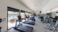 Located at 3470 Lee Cir in Prescott, Arizona, this well-appointed fitness center offers a comprehensive workout environment designed to accommodate a wide range of exercise routines. The single-floor space is generously sized, with vaulted ceilings that contribute to an open, airy atmosphere throughout.

The cardio zone is equipped with multiple treadmills, elliptical trainers, and stationary bikes from Life Fitness, all positioned along a wall of large, floor-to-ceiling windows. These expansive windows flood the space with natural light and provide direct views of the outdoor pool deck, complete with lounge chairs and vibrant yellow umbrellas, creating an energizing backdrop for workouts.

The strength training area features a multi-station cable machine, a dedicated TRX Training Zone with suspension straps and weighted accessories, a rack of dumbbells, and wall-mounted mirrors that enhance the sense of space. Posted fitness guidelines and safety equipment, including an AED, reflect a commitment to user safety.

The flooring throughout is durable, cushioned gym-grade material, ideal for both cardio and strength activities. The space is well-lit with recessed lighting, climate-controlled, and includes a mounted television for entertainment. Direct access to the outdoor pool and patio area makes this fitness center a seamlessly integrated part of the broader amenity offering.