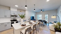 This well-appointed 2-bedroom, 2-bathroom residence in Round Rock, TX offers a thoughtfully designed single-floor layout with modern finishes and an open, airy feel. The heart of the home is a striking open-concept kitchen and living area, where light gray shaker cabinets, white quartz countertops, and a classic subway tile backsplash create a clean, contemporary aesthetic. Stainless steel appliances, including a French door refrigerator, microwave, and electric range, round out the kitchen's functionality. A spacious island with bar seating and sleek pendant lighting serves as both a prep space and gathering spot, flowing seamlessly into the living and dining areas, which benefit from natural light and access to an outdoor area via a glass door. Light wood-style flooring runs throughout the main living spaces, complemented by a ceiling fan overhead. The primary bedroom features a walk-in closet and an en-suite bathroom with gray vanity cabinetry, white quartz counters, and a glass-enclosed shower. The second bedroom showcases a bold accent wall and ample natural light. A second full bathroom with a built-in mudroom-style entry nook adds everyday practicality. Both closets offer generous shelving and hanging storage, making this a highly functional and stylish home.