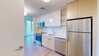 Located in Baltimore, MD 21231, this thoughtfully designed studio offers a efficient and modern single-floor layout encompassing one bedroom, one bathroom, a kitchen, a dedicated closet, and in-unit laundry. Light hardwood-style flooring runs throughout, lending warmth and visual continuity to the space.

The kitchen is well-appointed with a full suite of stainless steel appliances, including a refrigerator, dishwasher, electric range with oven, and an over-the-range microwave. Crisp white cabinetry is complemented by warm wood-toned upper cabinets, open glass shelving, and a clean white countertop with an undermount sink — creating a functional yet stylish cooking space.

The bedroom is generously proportioned and features expansive floor-to-ceiling windows that frame sweeping urban views of the Baltimore skyline, flooding the room with abundant natural light. A dedicated walk-in closet with built-in shelving provides ample storage.

The bathroom is finished in a clean, contemporary style with large-format white tile flooring, a floating wood-grain vanity with a white countertop, and a glass-enclosed walk-in shower accented by a striking stone tile feature wall.

Overall, the space presents a bright, modern aesthetic with clean lines and quality finishes throughout.