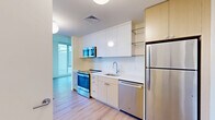This contemporary 430 square foot studio apartment in Baltimore, MD showcases a thoughtful design that maximizes space and light. The main living area is highlighted by expansive floor-to-ceiling windows, offering sweeping views of the urban landscape and flooding the space with natural light. The open-concept layout seamlessly integrates living and sleeping areas, enhanced by light-toned hardwood flooring that adds warmth and continuity throughout.

The kitchen, though compact, is efficiently designed with modern stainless steel appliances, including a full-sized refrigerator and dishwasher. White cabinetry and countertops maintain a clean, minimalist aesthetic, while a built-in microwave and ample storage optimize functionality.

The bathroom features a sleek design with a glass-enclosed shower, modern vanity, and large mirror. Light-colored tiles and fixtures contribute to a bright, spacious feel. A walk-in closet provides generous storage space, a valuable asset in a studio layout.

The apartment's neutral color palette, predominantly white walls, and ceilings create an airy ambiance that complements the city views. Recessed lighting and a centrally placed pendant light fixture offer versatile illumination options. This studio epitomizes urban living, balancing style, efficiency, and comfort in a compact yet well-appointed space.