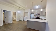 This thoughtfully designed one-bedroom unit offers a comfortable and functional single-floor layout with modern finishes throughout. The open-concept kitchen and living area serves as the heart of the home, featuring stainless steel appliances including a refrigerator, range, microwave, and dishwasher, complemented by soft gray cabinetry, white countertops, and a peninsula island with pendant lighting overhead. Durable wood-look flooring runs throughout the main living areas, adding warmth and continuity to the space. A glass-paneled exterior door in the living area allows natural light to fill the room. A dedicated in-unit laundry closet with a full-size washer and dryer provides added convenience. The generously sized bedroom features plush carpeting, a bright window with blinds, and direct access to a walk-in closet outfitted with dual hanging rods and ample shelving. The hallway connecting the living area to the bedroom is accented by a statement pendant light fixture, while a full bathroom with vanity and mirror is conveniently accessible. Neutral tones, clean lines, and well-placed lighting create a cohesive and inviting ambiance throughout the entire space.