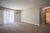 Located at 3362 Woodward Ave SW in Wyoming, Michigan, this single-floor unit offers a practical and comfortable layout designed for everyday living. The kitchen is equipped with warm-toned wood cabinetry, granite countertops, wood-look vinyl flooring, and white appliances including an electric range, over-the-range microwave, and refrigerator. A baseboard heating unit lines the kitchen wall, and the open layout connects seamlessly to the rest of the unit. The living area features neutral-toned carpet, soft gray walls, and a sliding glass door fitted with vertical blinds that brings in natural light and provides outdoor access. A wall-mounted air conditioning unit and baseboard heating ensure year-round comfort. The bedroom is generously sized with plush carpeting, a window overlooking greenery, and chair-rail-style wainscoting detail along the walls. An additional carpeted room with recessed lighting and a wall AC unit offers flexible use as a second bedroom or office. The full bathroom is clean and well-appointed, featuring a tub/shower combo, a wood vanity with granite countertop, and wood-look vinyl flooring. Throughout the unit, the design maintains a consistent, neutral palette with functional finishes that create a cohesive and livable environment.