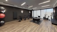 This contemporary fitness center is thoughtfully designed to accommodate a wide range of training styles and fitness goals. The space features warm wood-look flooring throughout, set against dark charcoal accent walls that give the gym a sleek, professional aesthetic. Linear LED lighting runs across the ceiling, providing bright, even illumination throughout the facility.

The main workout floor is generously proportioned, offering ample room for both equipment use and functional training. A dedicated functional training zone features a heavy flip tire and padded mat, ideal for high-intensity workouts. Along the windowed wall, floor-to-ceiling frosted glass panels allow diffused natural light to fill the space while maintaining privacy. This area houses a Concept2 rowing machine, an air bike, and multiple treadmills, complemented by a large wall mirror that enhances the sense of depth.

A row of Schwinn spin bikes lines another section of the gym, positioned in front of a large flat-screen display and built-in shelving stocked with medicine balls and accessories in a rich red-accented niche. A dumbbell rack with color-coded weights and an additional monitor provide a well-organized free weights station.

Glass-panel sliding doors open to a connected studio or stretching area, adding versatility to the overall layout. Wall-mounted sconce lighting adds a refined touch throughout, elevating the ambiance beyond a typical fitness facility.